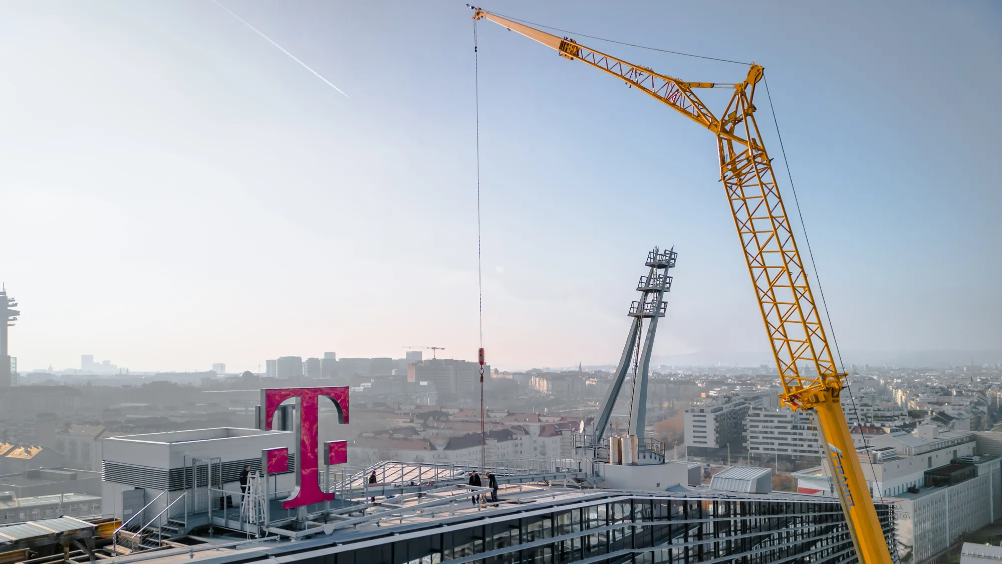 Drohnenaufnahme einer Baustelle auf einem Dach mit Telekom-Logo und Baukran in Wien