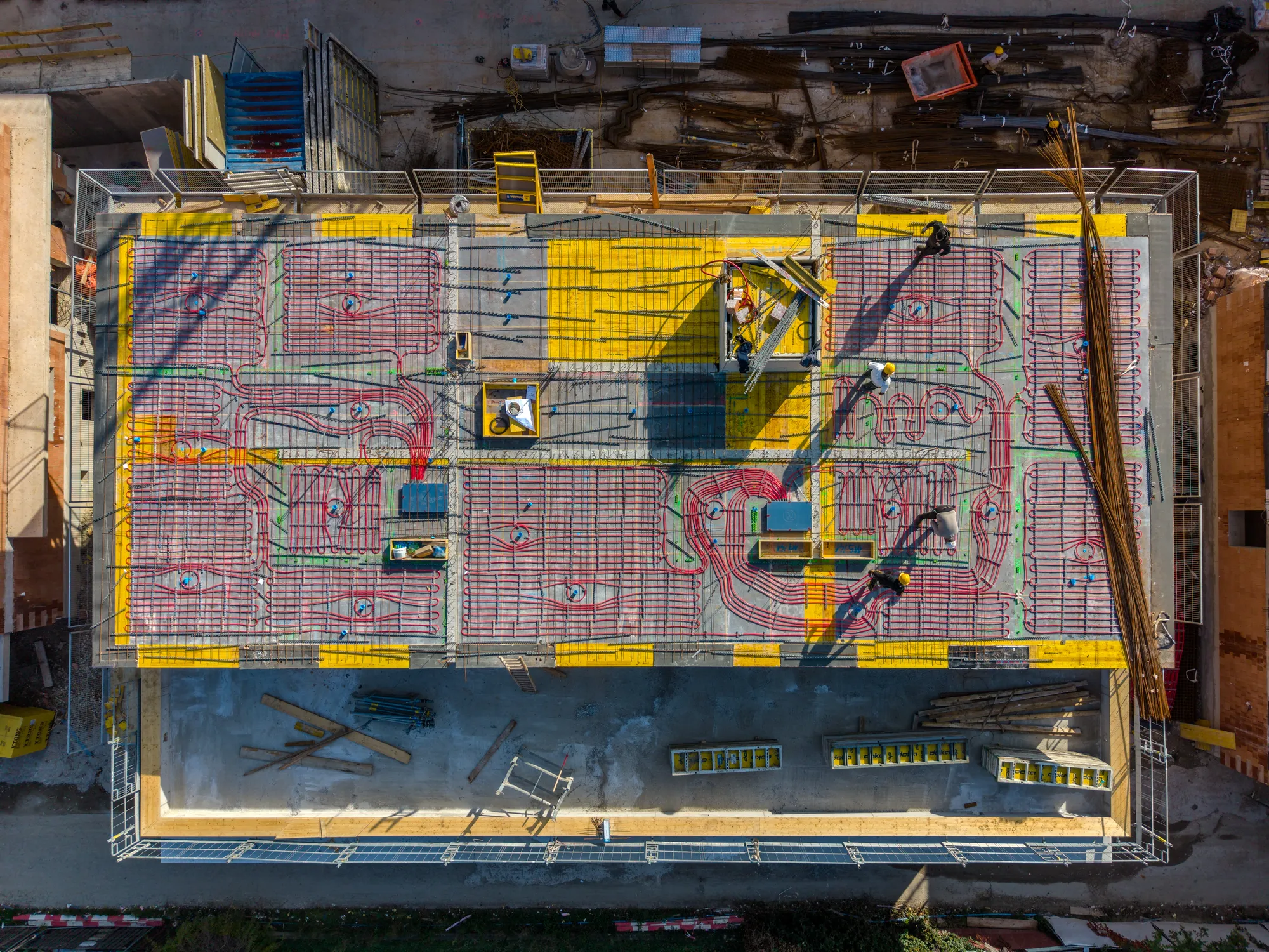 Senkrechte Drohnenaufnahme einer Baustelle: Rohbau-Deckenplatte mit Bewehrung und verlegten Installationsleitungen, Arbeiter auf der Konstruktion.